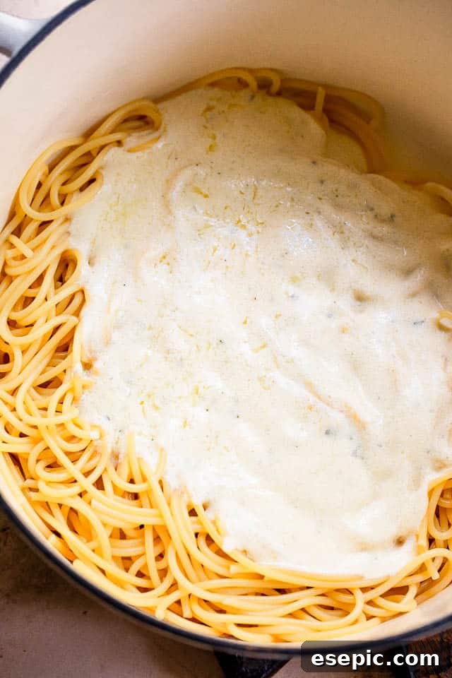 White dutch oven with spaghetti and white cream sauce on top, being stirred