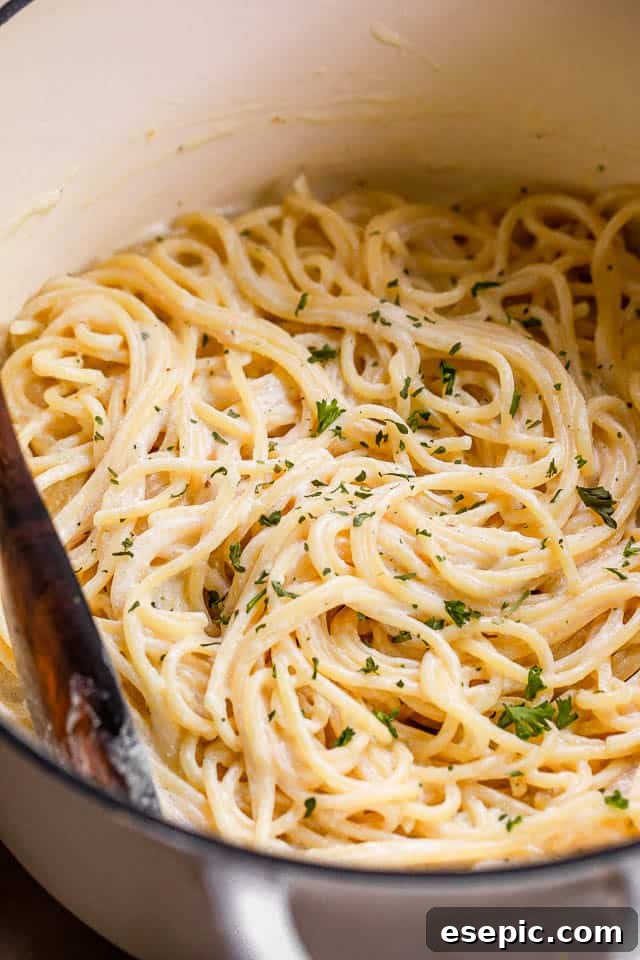 Cooked spaghetti in a white dutch oven, coated in creamy sauce, with a serving spoon