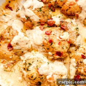 top view of cooked cream sauce chicken thighs in a white skillet with a silver serving spoon picking up the food