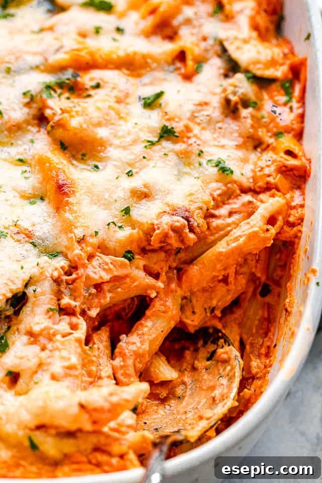 Velvety Zucchini Mushroom Pasta Bake 5 A side view of the cheesy pasta bake in a baking dish, with a serving spoon lifting out a portion, showing the layers of pasta, vegetables, and melted cheese.