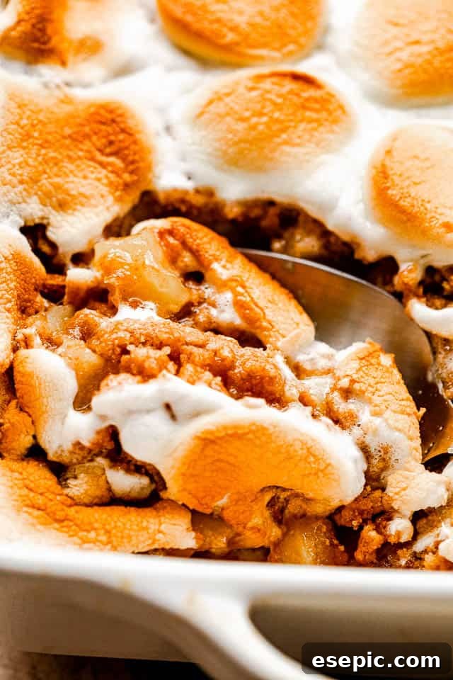 S'mores-Inspired Apple Crumble 7 A slice of marshmallow-topped apple crumble being lifted from the baking dish with a serving spoon, showcasing its gooey interior.