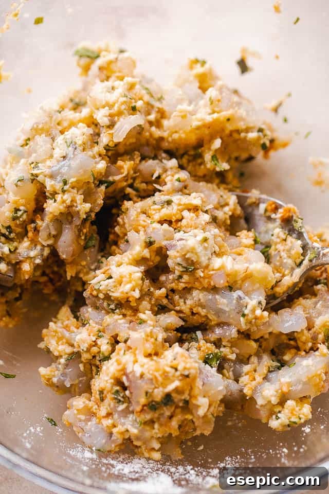 Crispy Coconut Shrimp Fritters 4 A bowl of the raw mixture for coconut shrimp cakes, showing chopped shrimp, panko, coconut, and herbs mixed together.
