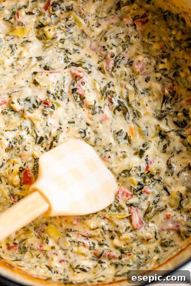 A spatula stirring the creamy, vibrant slow cooker spinach artichoke dip in a slow cooker, highlighting its rich texture.