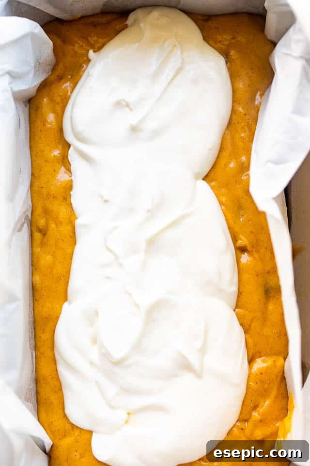 A golden-orange pumpkin bread batter, complete with walnuts and raisins, poured into a loaf pan, ready for the creamy swirl and baking.