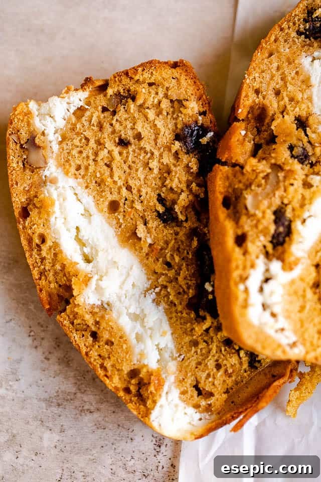 A close-up side view of a thick slice of Pumpkin Swirl Bread, showcasing the vibrant pumpkin bread intertwined with the creamy white cheese filling.