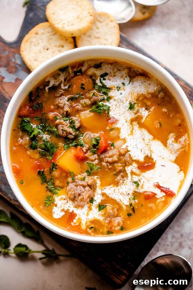 A rich and comforting soup prepared with spicy and bold Italian sausage, tender white beans, tangy diced tomatoes, and a base of pureed butternut squash. Overhead shot of butternut squash and sausage soup served in a white bowl, ready to eat.