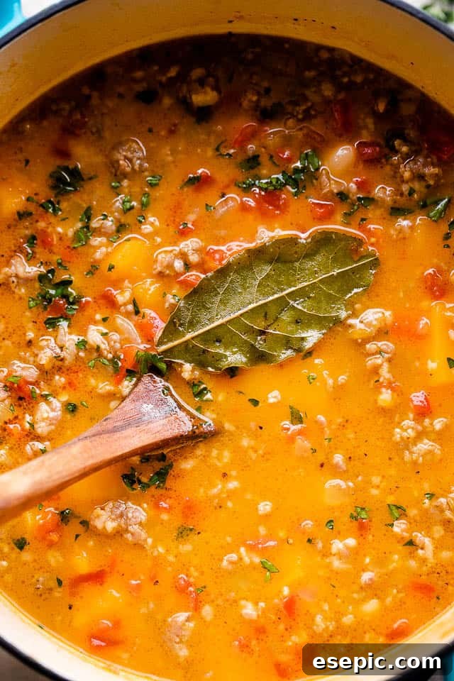 A rich and comforting soup prepared with spicy and bold Italian sausage, tender white beans, tangy diced tomatoes, and a base of pureed butternut squash. Overhead, close-up image of butternut squash soup cooking in a Dutch oven, showing the rich texture and vibrant colors.