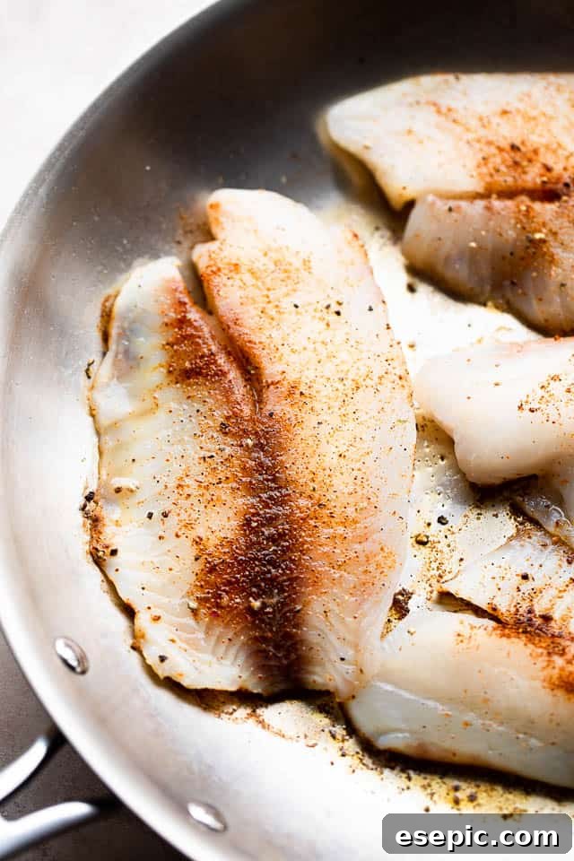Tilapia fillets being cooked to a golden crisp in a hot skillet, ready for the creamy tomato sauce.