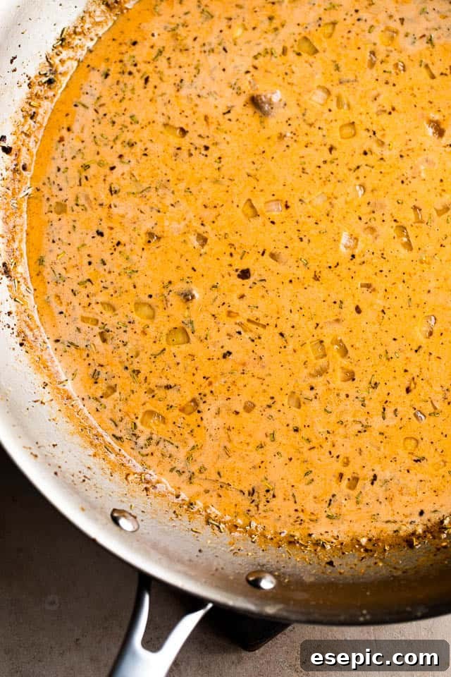 The creamy tomato sauce simmering gently in a stainless steel skillet, rich with butter, onions, garlic, and Italian herbs.