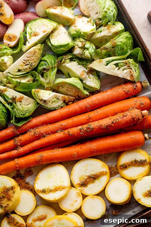 Raw carrots, Brussels sprouts, squash, and potatoes on a baking sheet, coated in balsamic vinaigrette