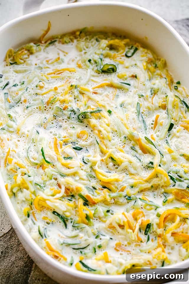 Golden Zucchini Squash Gratin 4 Overhead shot of an unbaked zucchini and squash casserole, showing layers of spiralized vegetables, cream sauce, and cheese, ready for the oven