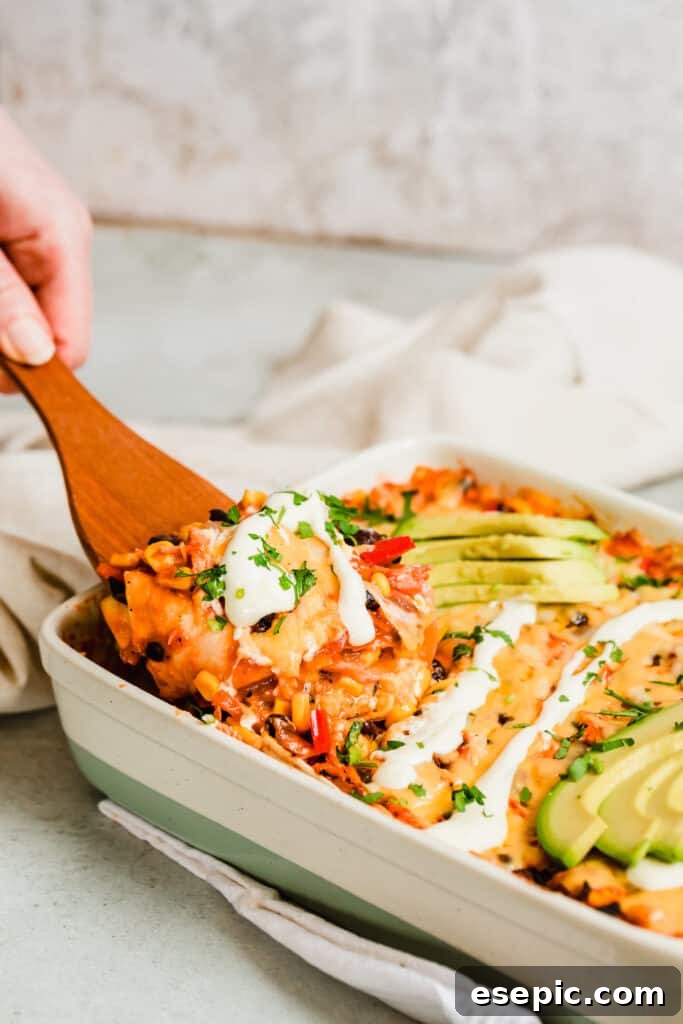 A wooden spoon scooping into a golden, bubbly Chicken Enchilada Casserole fresh from the oven, showing layers of tortillas, chicken, and cheese.