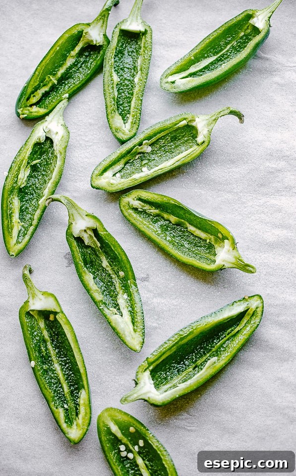 Creamy, spicy, crunchy Bacon Wrapped Jalapeño Poppers are stuffed with cheese and wrapped in bacon. The perfect Super Bowl food idea! Halved and seeded fresh jalapeños arranged neatly on a parchment-lined baking surface, ready for filling.