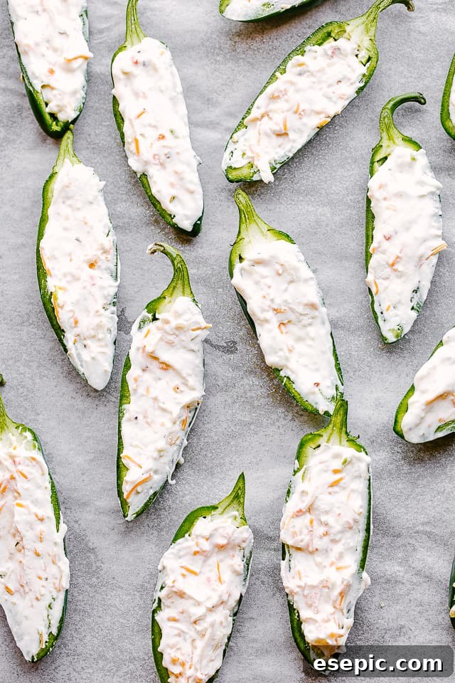 Creamy, spicy, crunchy Bacon Wrapped Jalapeño Poppers are stuffed with cheese and wrapped in bacon. The perfect Super Bowl food idea! Raw jalapeño halves, perfectly stuffed with the creamy shredded cheese mixture, showcasing preparation before baking.