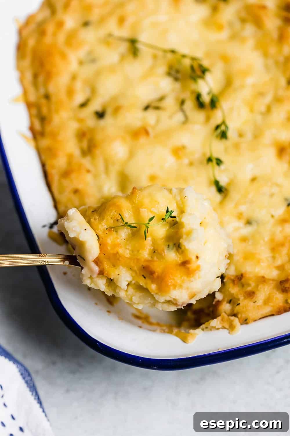A spoon scooping baked mashed potatoes out of a casserole dish.