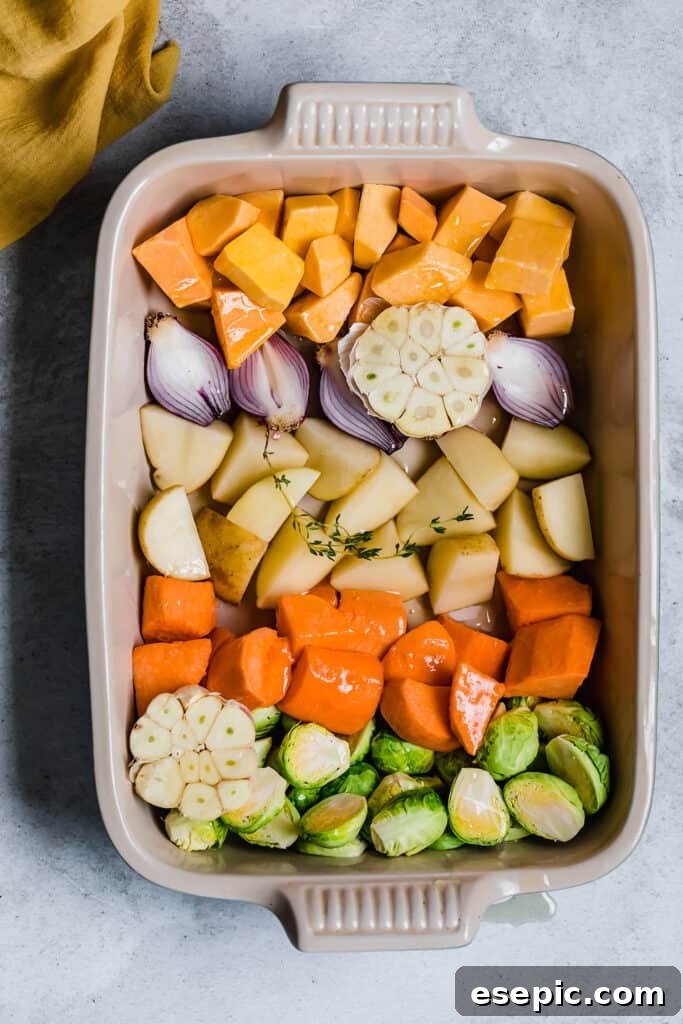 Assortment of chopped root vegetables tossed with olive oil and fresh thyme sprigs in a roasting pan, ready for the oven.