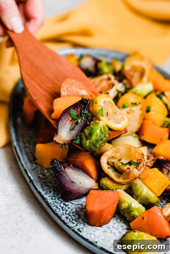 A wooden spoon delicately scooping golden roasted vegetables from a blue serving platter, highlighting their texture.