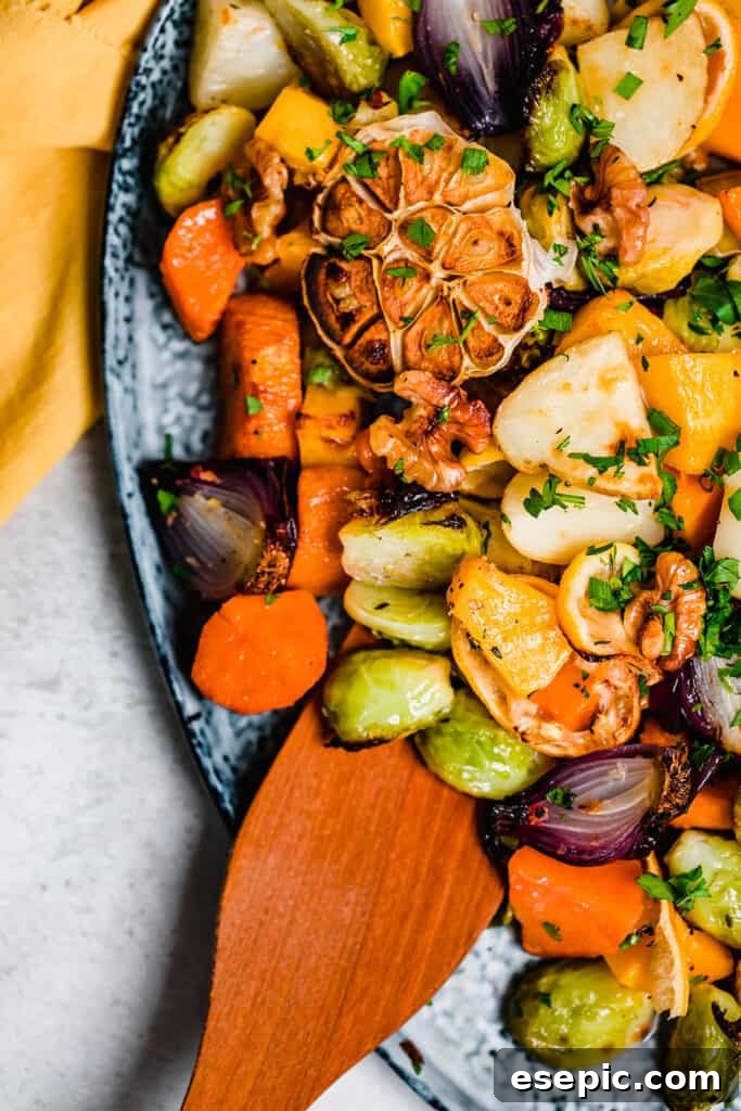 A wooden spoon resting on a bed of glistening roasted root vegetables and Brussels sprouts on a blue serving platter.