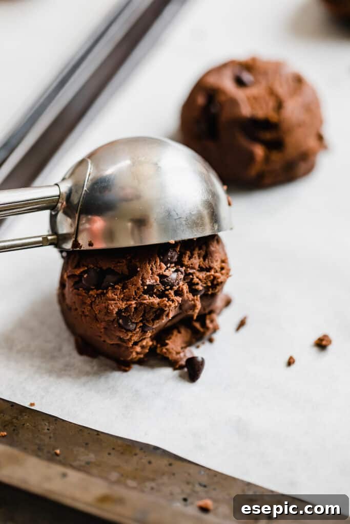 Cozy Cocoa Sugar Cookies 9 A metal ice cream scoop releasing a ball of chocolate sugar cookie dough onto parchment paper.