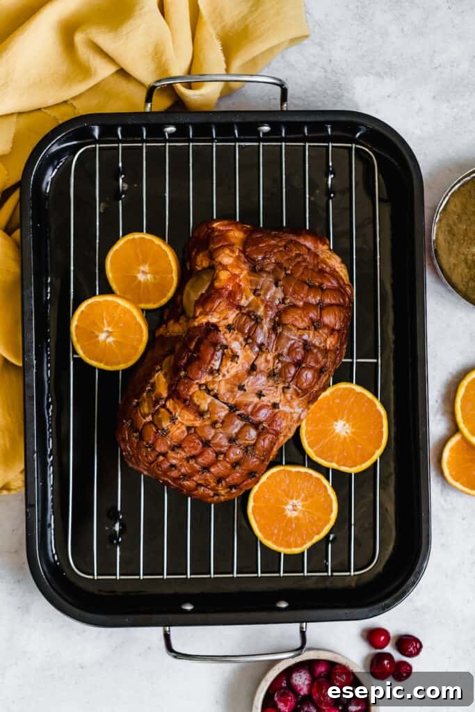 A Christmas Ham placed on a roasting pan, surrounded by orange slices, ready for baking.