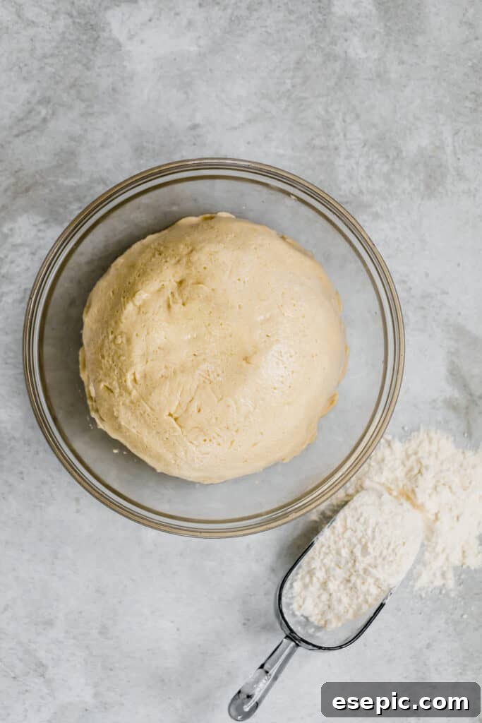The Dinner Roll Dough in a Glass Bowl Beside a Scoop with Flour Inside It