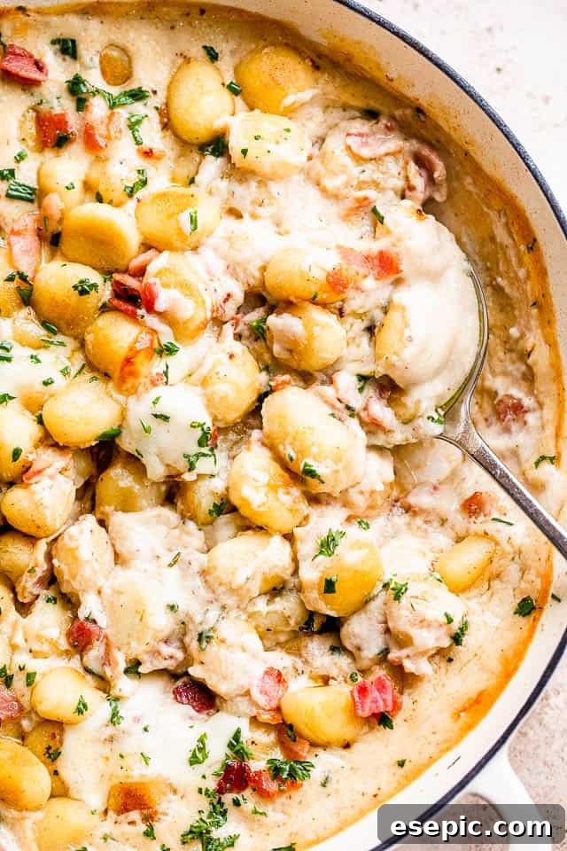 Golden Gnocchi and Crispy Bacon Bake 6 A serving spoon lifting a generous portion of creamy gnocchi and bacon casserole from a baking dish