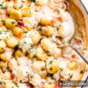 Golden Gnocchi and Crispy Bacon Bake 7 A serving spoon lifting a generous portion of creamy gnocchi and bacon casserole from a baking dish