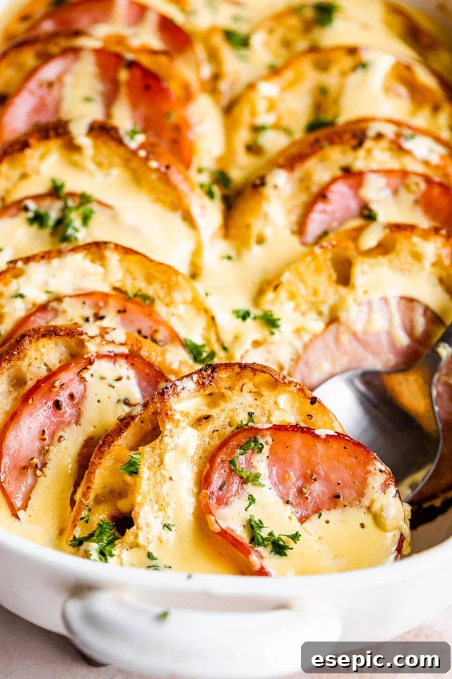 Spoonful of golden brown Eggs Benedict Casserole being served from a baking dish, topped with Hollandaise sauce.