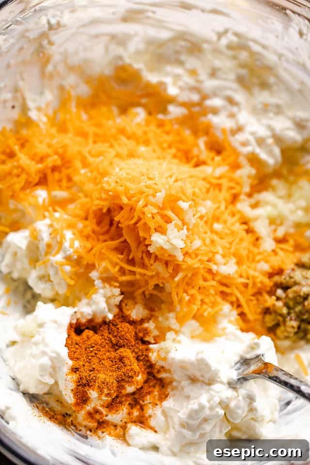Creamy Baked Crab Dip 3 A bowl filled with cream cheese, sour cream, mayonnaise, seasonings, and shredded cheddar cheese, ready to be mixed for hot crab dip.