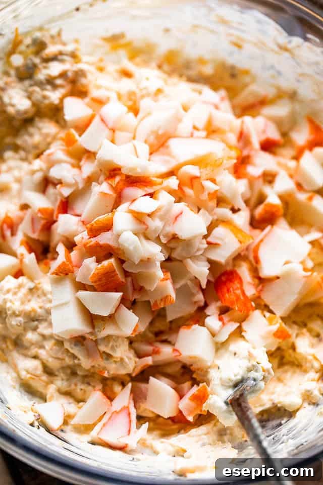 Creamy Baked Crab Dip 4 A close-up of a spoon gently mixing lump crab meat into a creamy cheese base in a large mixing bowl.