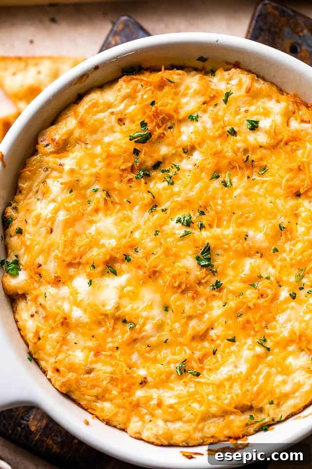 Creamy Baked Crab Dip 5 An overhead shot of a white skillet brimming with golden, bubbly hot crab dip, garnished with fresh herbs.
