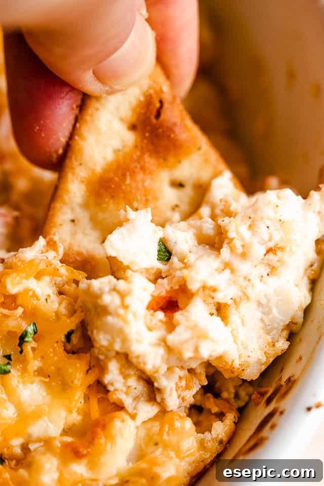 Creamy Baked Crab Dip 6 A pita chip being dipped into a warm, creamy hot crab dip, showing the rich texture and melty cheese.