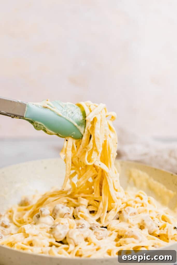 A Pair of Tongs Grabbing a Bunch of Fettuccine Noodles Covered in Alfredo