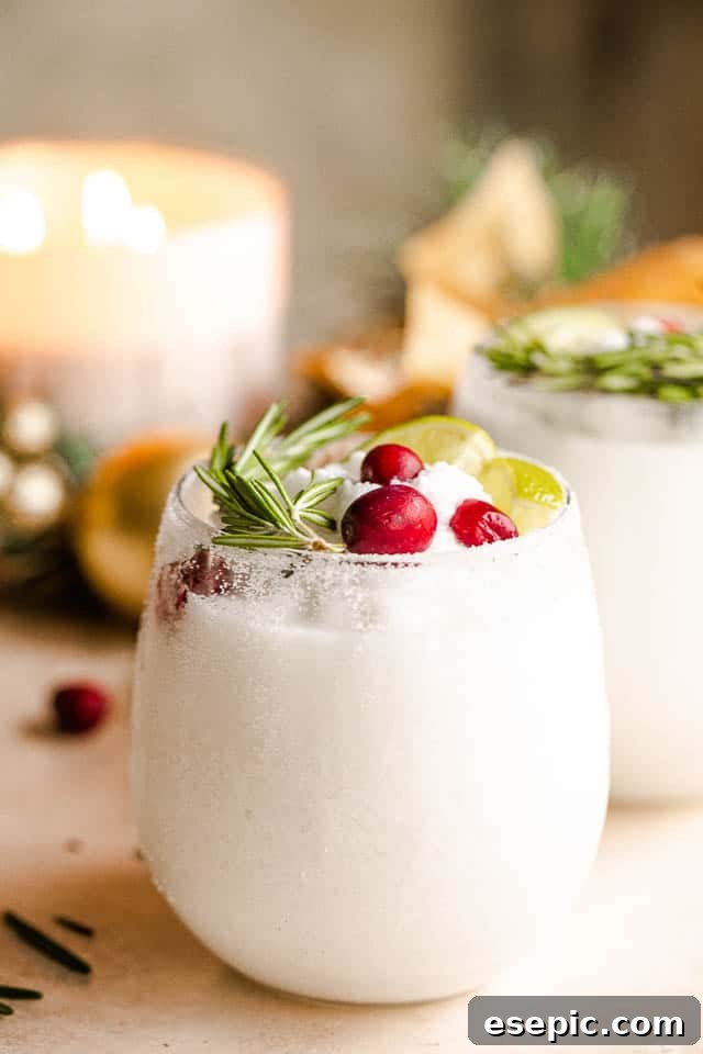 Frozen Christmas Margaritas: Tequila, Triple Sec, and Coconut Milk Bliss Festive drinking glasses filled with white frozen margaritas, garnished with vibrant lime slices, fragrant rosemary sprigs, and ruby-red cranberries, evoking a snowy winter scene with a tropical twist.