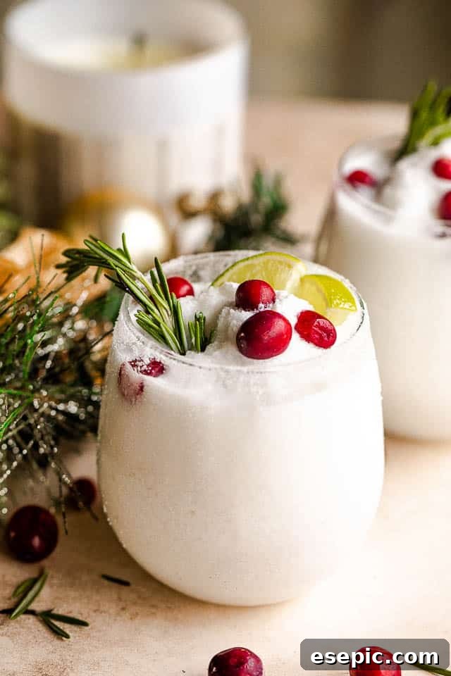 The perfect blend of coconut milk, tequila, triple sec, and lime for holiday cheer. Beautifully presented Frozen Christmas Margaritas in elegant drinking glasses, adorned with slices of lime, sprigs of fresh rosemary, and bright red cranberries, ready for a festive celebration.