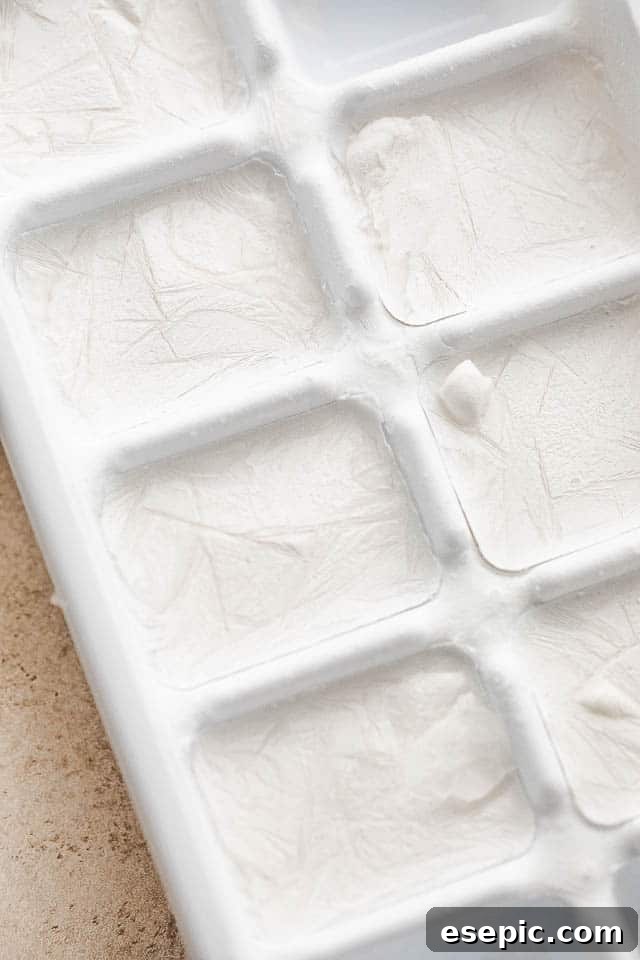 The secret to creamy frozen margaritas: coconut milk ice cubes. Ice cube tray filled with white frozen coconut milk cubes, ready for blending into a delicious frozen margarita.
