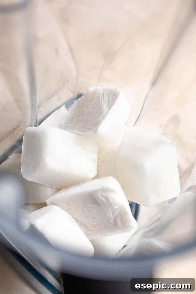 Blending the magic: coconut milk ice cubes for holiday cocktails. Close-up of a blender pitcher containing creamy white coconut milk ice cubes, poised to be transformed into festive frozen margaritas.
