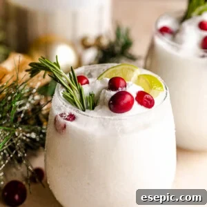 Drinking glass filled with festive margaritas, garnished with lime, rosemary, and cranberries.