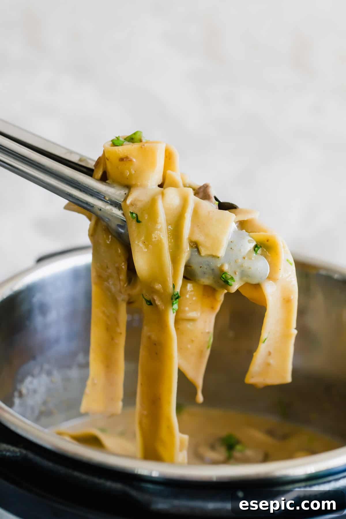 A Pair of Tongs Pulling a Scoop of Beef Stroganoff Out of the Instant Pot