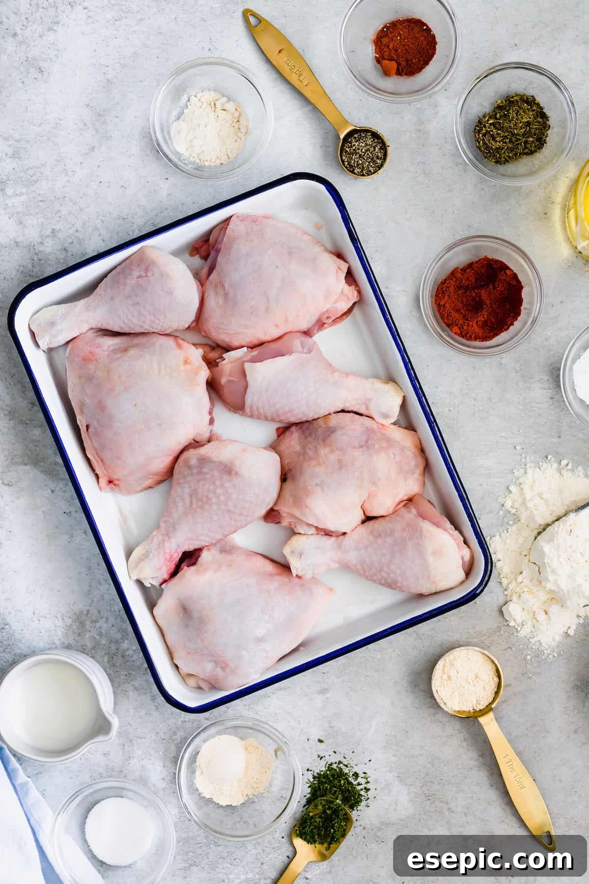 Eight Chicken Thighs and Drumsticks in a White and Blue Pan Surrounded by Herbs, Spices and Buttermilk