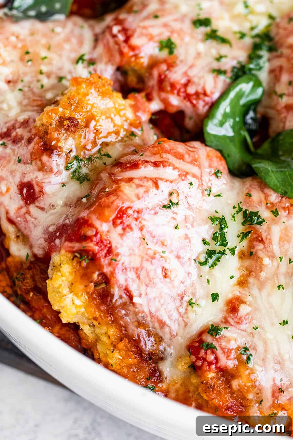 close up shot of baked pork parmigiana topped with melted cheese and basil leaves.