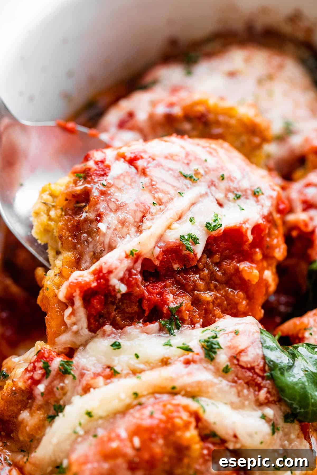 spooning out baked pork parmigiana medallions from baking dish.