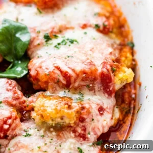 close up side shot of baked pork parmigiana topped with melted cheese and basil leaves.