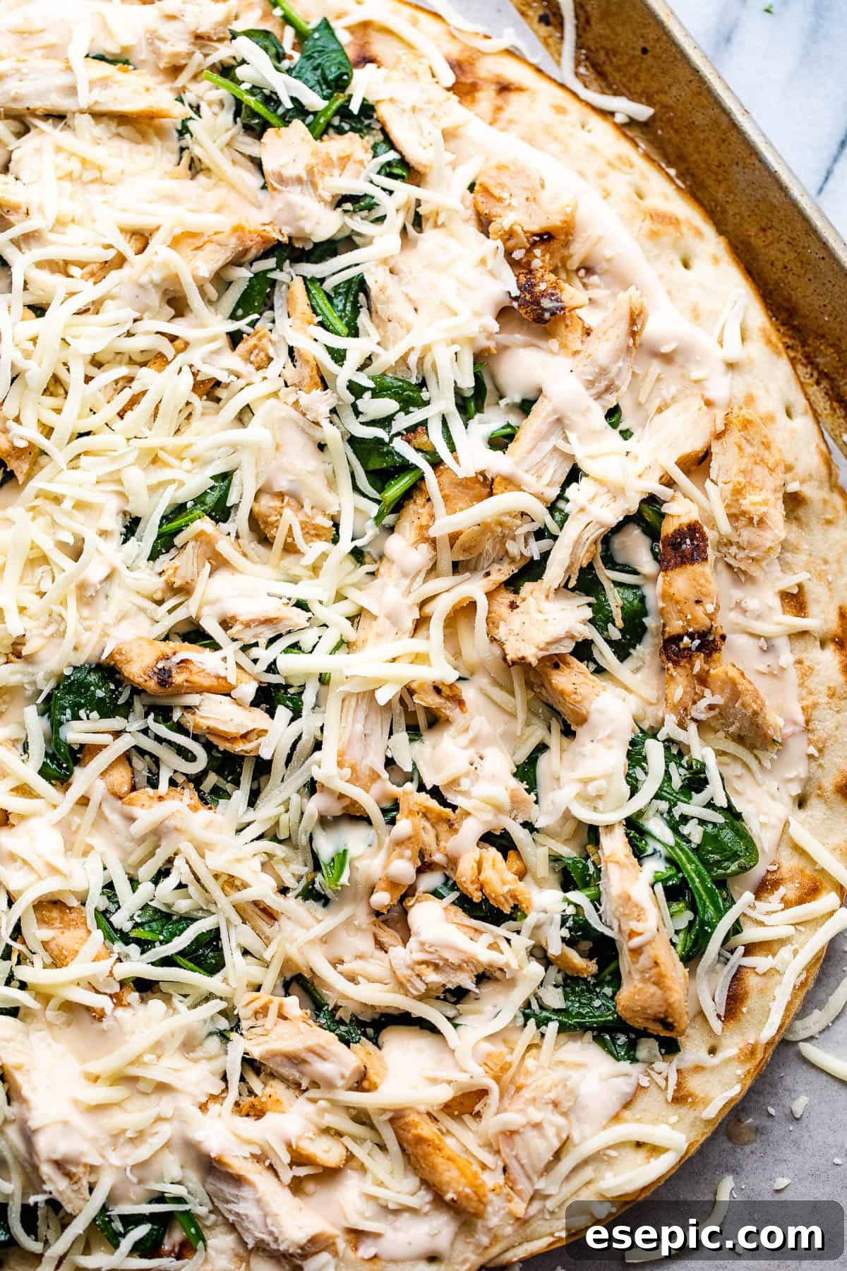 Assembling a delicious pizza with Alfredo sauce, shredded chicken, sautéed spinach, and shredded cheese.