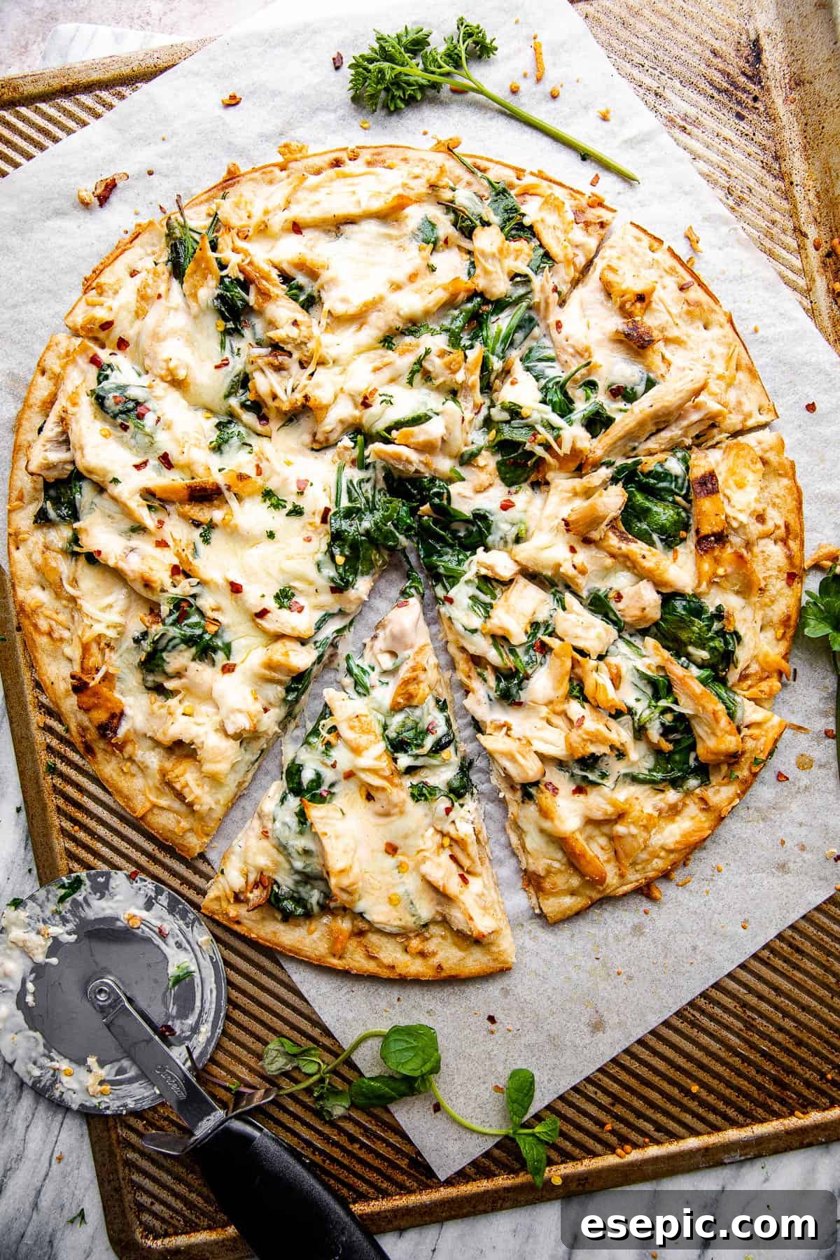 An overhead shot of a freshly baked homemade Chicken Alfredo Pizza, with a pizza cutter resting beside it, ready to be sliced.