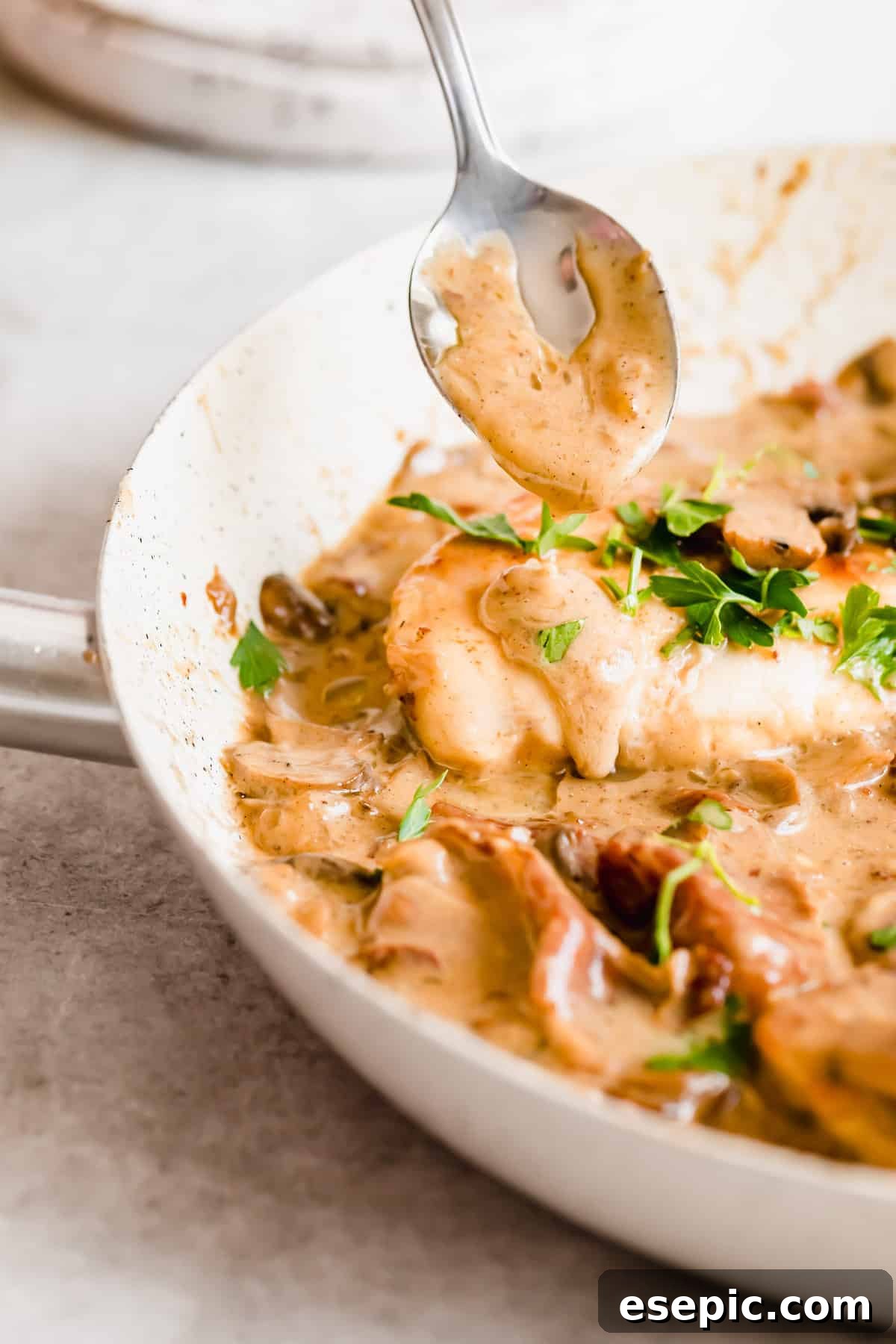 Luscious Marsala Chicken 8 A wooden spoon pouring rich, creamy marsala sauce over a piece of chicken, garnished with fresh herbs.