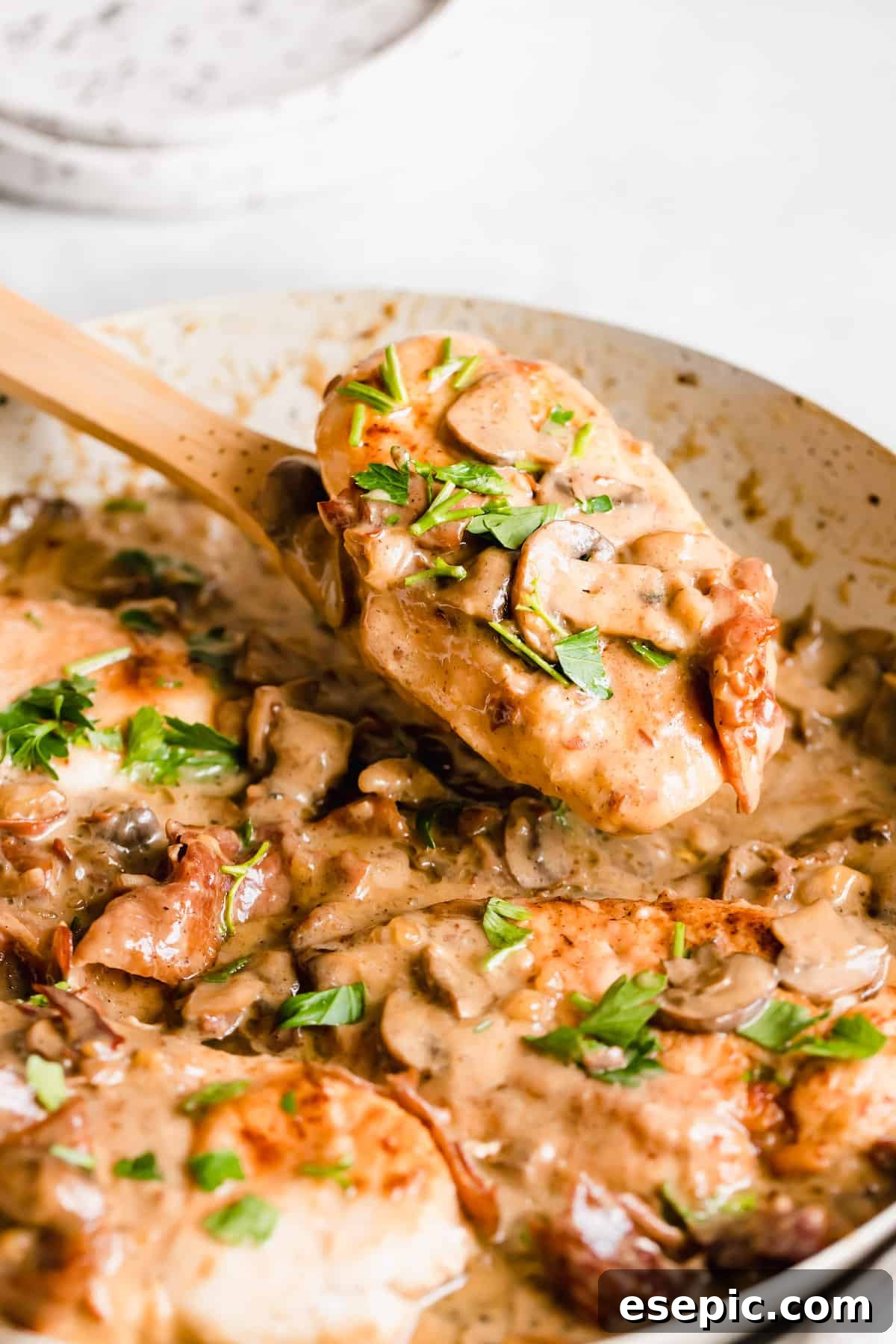 Luscious Marsala Chicken 9 A single piece of creamy chicken marsala, perfectly sauced, on a wooden serving spoon, garnished with fresh herbs.