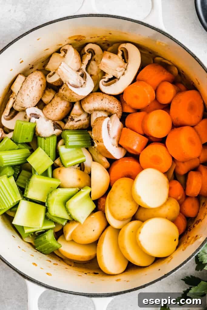 Slow-Simmered Guinness Beef Stew 9 A colorful array of chopped raw celery, carrots, onions, potatoes, and mushrooms layered in a large soup pot, ready to be cooked down for a hearty stew.