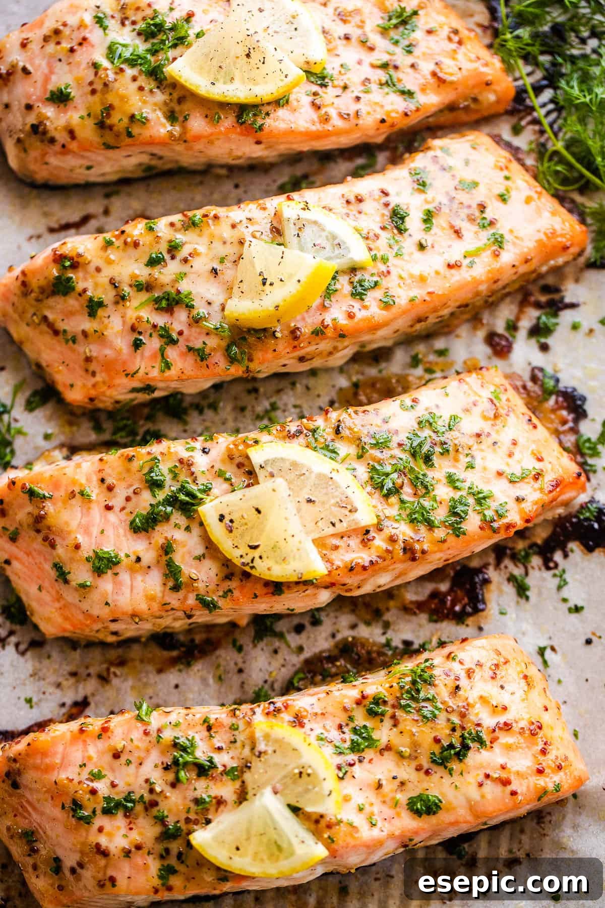 This baked Maple Mustard Salmon recipe is lightly seasoned, then brushed with a sweet and tangy sauce made from maple syrup and Dijon mustard! four baked maple mustard salmon fillets on a baking sheet, golden and glistening