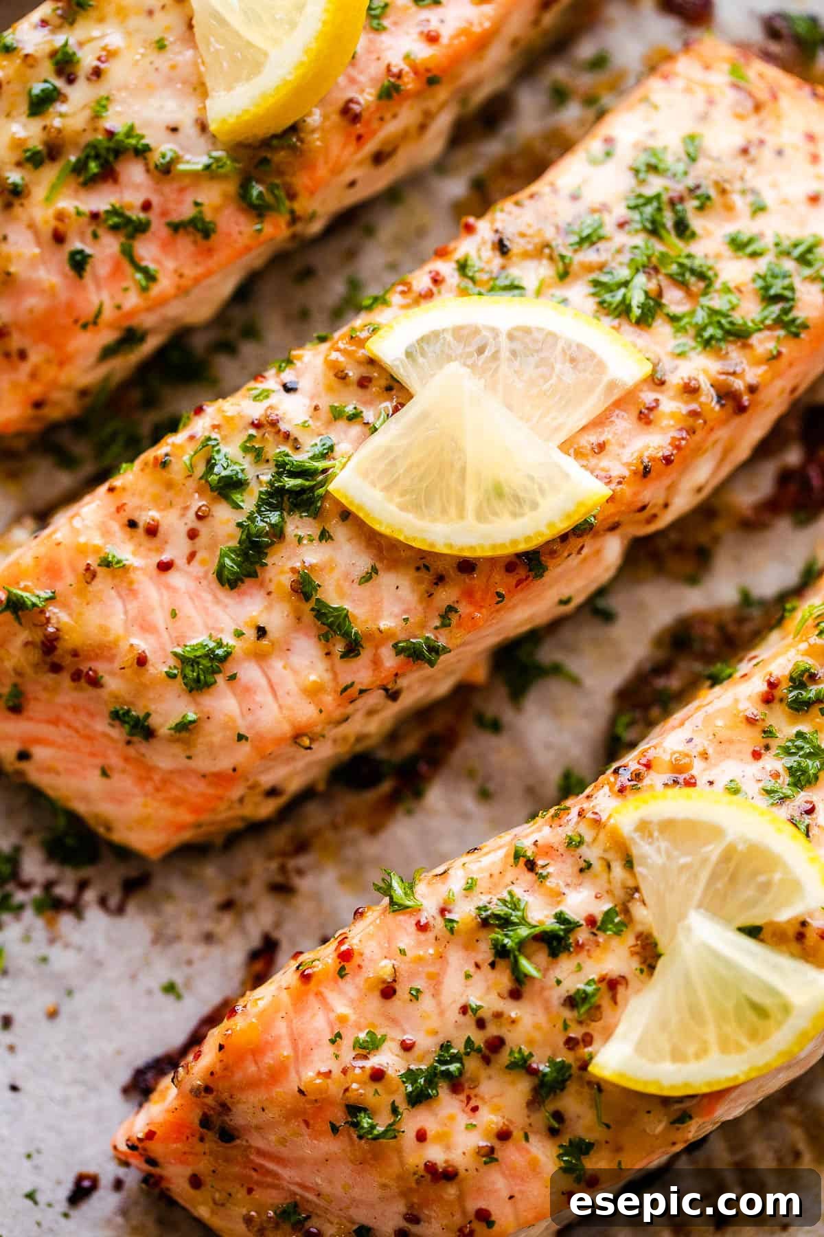 This baked Maple Mustard Salmon recipe is lightly seasoned, then brushed with a sweet and tangy sauce made from maple syrup and Dijon mustard! up close photo of maple mustard salmon fillets garnished with fresh parsley and vibrant lemon slices